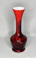 Photo of red and black swirled Italian opaline glass vase with a flared neck and white interior, standing against a plain background.