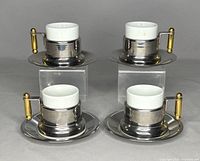 Set of four assembled espresso cups on stainless steel saucers with brass-handled cupholders