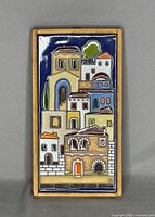 Front view of the rectangular glazed pottery tile depicting stylized Greek buildings with various roof shapes and colors against a dark blue background, framed with a yellowish border.