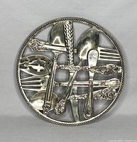 Full top view of the round silver plated trivet with decorative cutlery pattern