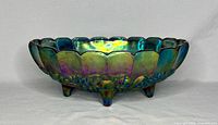 Side view of vintage blue iridescent carnival glass bowl with grape motif on five feet.