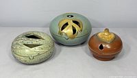 Photo showing all three pottery vessels side by side with visible glaze, texture, and cut-out designs.