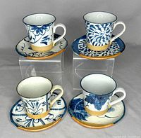 Four vintage Japanese stoneware cups and saucers displayed on clear stands, showing various hand-painted blue and white patterns with natural textured bands near base.