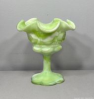 Front view of the green and white slag glass footed compote showing crimped ruffled rim.