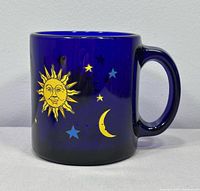 Front view of cobalt blue glass mug showing yellow sun, crescent moon and stars design