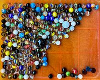 Vintage marbles of mixed colors and sizes arranged on an orange grid surface.