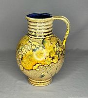 Front side view of the rounded jug with handle showing textured yellow and beige crackled glaze and dark blue interior.
