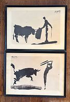 Photo showing two lithographs with bulls and toreros in minimal black silhouette style, framed