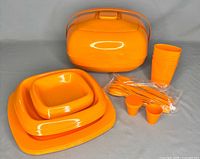 Full view of the orange 4-person picnic set with plates, bowls, cups, utensils, egg cups and carrying container arranged on gray background.
