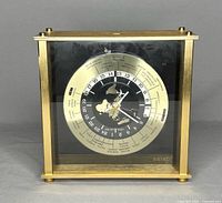 Front view of a square brass-tone metal framed clock with glass face. Shows Seiko branding and world time zones.