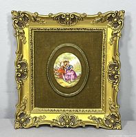 Full view of the framed wall art showing the entire ornate gold frame, velvet background, and central porcelain plaque with the courting couple scene.