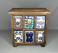 Front view of the vintage wood apothecary cabinet showing six porcelain drawers with colorful hand-painted designs.