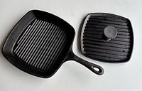 Square cast iron ribbed grill pan with matching ribbed lid for panini pressing shown from angled side view.