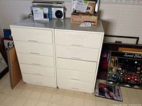 Two white 5-drawer melamine cabinets placed side by side. Some items are stacked on top but not part of the lot.