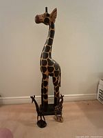 Three wooden giraffe sculptures of varying sizes positioned on a carpeted floor against a wall, showing relative scale.