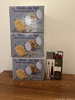 Three boxes of 2-piece Glass Jar Sets with Stainless Steel Lids stacked, showing packaging details.