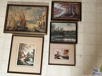 Overview of the five framed artworks arranged on the floor showing variety in size and subject matter.