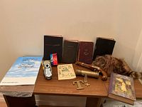 Collection of vintage and antique books plus assorted vintage items on wooden table against beige wall.