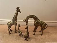 Family of four brass giraffe figurines in descending height order displayed on carpet in front of white baseboard.