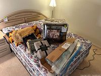 View of multiple blankets and throws laid out on a floral mattress including packaged queen sheet set and vacuum seal bags