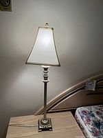 Photo of one lamp showing fabric shade turned on, positioned on a bedside table against wall.