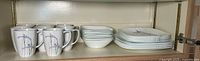 Shelved set of 8 Corelle iris pattern cups and square plates, cups on left and plates on right.