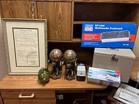 Full lot shown on wooden desk surface including framed document, piggy bank, bookends, keyboard box, filing box, pencil sharpener, and gloves.