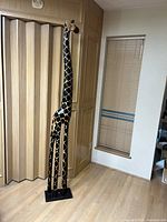 Full view of the 80 inch tall wooden giraffe figurine standing in a room, showing its height and shape.