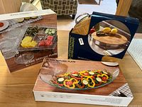Boxed set of eight clear glass serving plates visible, one large oval platter and several rectangular plates, alongside the chopping block box
