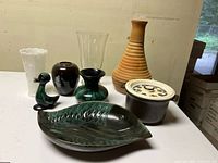 Wide view of assortment of pottery and glass items on white table including fish dish, vases, bird figurine, and casserole.