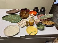 Overall assortment of pottery items on white surface including plates, bowls, cups, and decorative pieces in multiple colors and shapes.