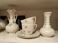 Overview of lot showing twin-handled vase, straight-neck vase, two teacups and two saucers