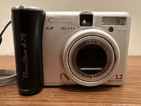Front view of Canon PowerShot A75 digital camera powered off showing branding, lens, and flash.