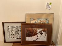 Three framed art prints stacked. Two Bev Doolittle prints, black and white forest scene and autumn track scene, plus Salvador Dali colorful surreal print behind them.