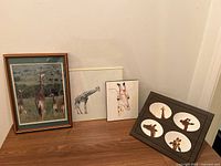 Four giraffe-themed framed art pieces arranged in a corner showing varied styles, including photo and illustrations on paper, framed in wood with glass