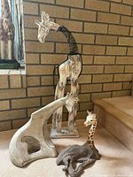 Photo showing all three giraffe figures grouped: a tall spring-neck wooden giraffe, a middle-sized light grey abstract giraffe, and a smaller detailed giraffe figure.