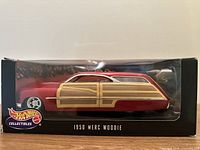 Front view of red 1950 Merc Woodie diecast car in display box with clear window, showing detailed wood paneling and chrome wheels