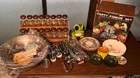 Photo of all vintage kitchen items displayed on dark wood table including boxed party fondue set, spice racks, hand beaters, wok, plates, and ashtrays.