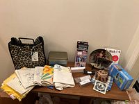 Wide photo of all lot items arranged on wooden table including Fit & Fresh chiller bag, linen towels, tin container, Closet Genie kit, collectors plate, coaster, basket, and turntable light.