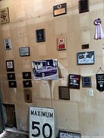 View of wall with multiple plaques, a Maximum 50 speed limit sign, vintage photographs and posters, and one purple ribbon.