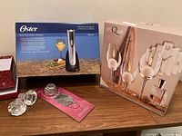 Lot items arranged showing original boxes of Oster electric wine opener and glass candle holders, two glass wine stoppers on card, pewter wine bottle decor