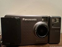 Front view showing silver Panasonic camera with lens and detachable flash attached on right side.