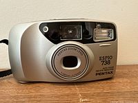 Front view of Pentax Espio 738 camera with zoom lens retracted, showing model name and lens specifications (f=38mm - 70mm).