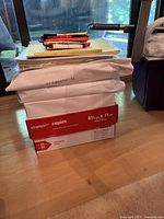 Photo showing box of Staples copy paper with legal pads and pens on top