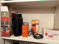 Shelf displaying all items: travel mug set in black zippered case alongside orange Braun coffee grinder and boxed Weight Watchers food scale.