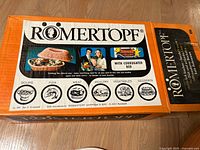 Photo of original product box showing Romertopf branding and cooking category icons for soups, fish, meat, poultry, vegetables, desserts.