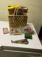 Overview of sewing kit items including basket with sewing supplies inside, scissors, pins, and needles.
