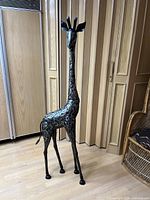 Full view of steel giraffe sculpture standing on wooden floor against folding door background