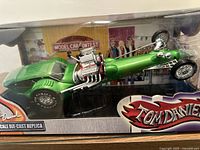 Front angle of green Tom Daniel dragster die-cast replica in box.