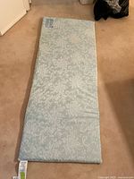 Full view of the light blue patterned magnetic bed topper lying on carpeted floor.